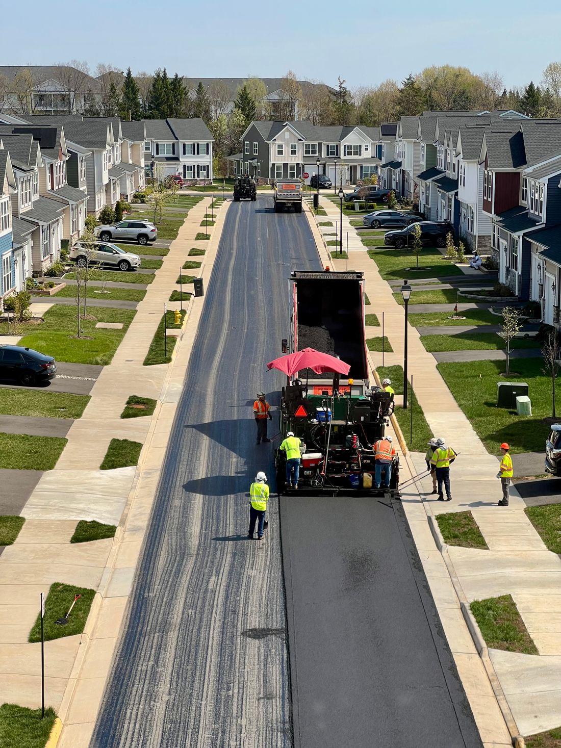 A paving crew laying a fresh strip of black asphalt down a residential street
