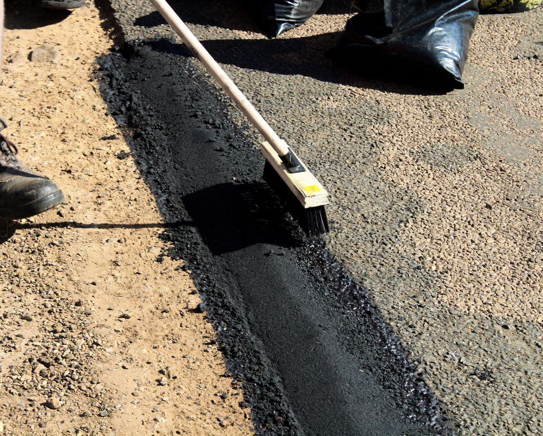 Fresh black asphalt being spread smooth along the edge of a drive