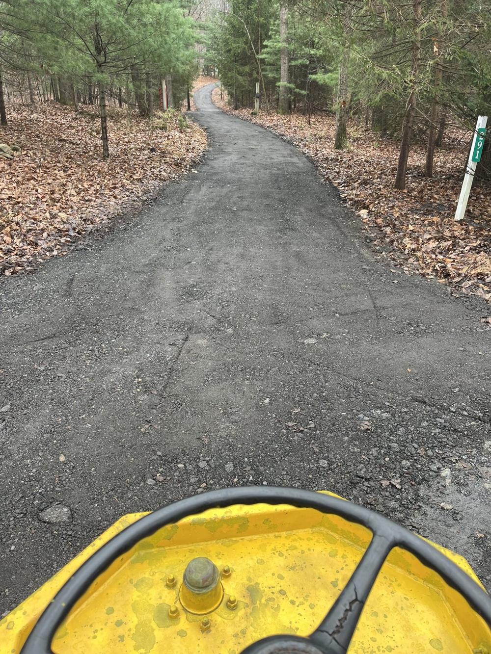 A long wooded driveway freshly surfaced by All About Asphalt, seen from the roller seat